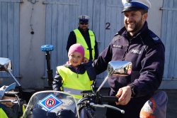 dziecko siedzi na motocyklu, stoi przy nim policjant, który się uśmiecha