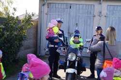 dziecko siedzi na motocyklu, przy nim po bokach policjanci - policjantka i policjant z dzieckiem na ręku