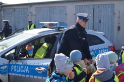 policjant częstuje dzieci cukierkami stojąc przed radiowozem