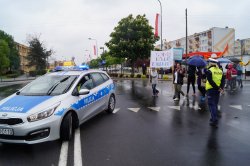 radiowóz pilotuje korowód idący ulicami Słupcy, skrzyżowanie na którym stoi policjantka