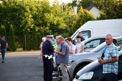 policjant rozdaje kamizelki, policjanci prowadzą akcję profilaktyczną  podczas święcenia pojazdów przed kościołem