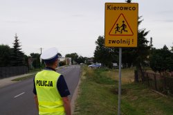 policjant drogówki na tle znaku KIEROWCO ZWOLNIJ