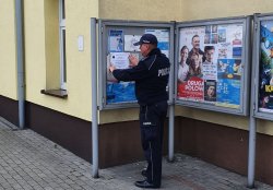 policjant przykleja plakat na tablicy ogłoszeń