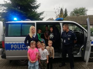 zdjęcie policjanta z grupą dzieci i wychowawców na tle radiowozu