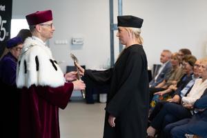 kobieta w birecie przyjmuje dyplom od mężczyzny rektora ubranego w czapkę i togę